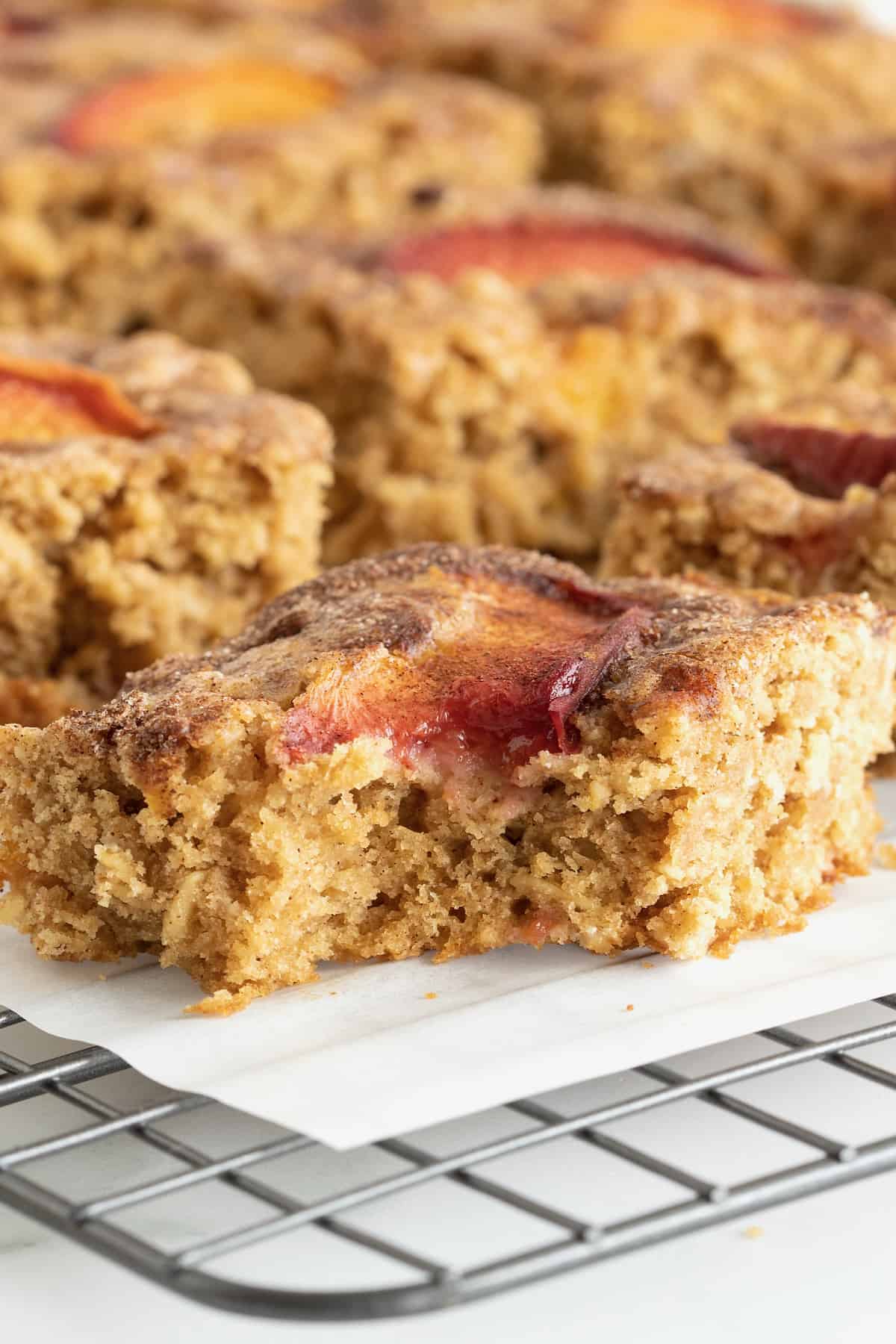 Oatmeal bars with peach slices on top resting on a parchment lined cooling rack.