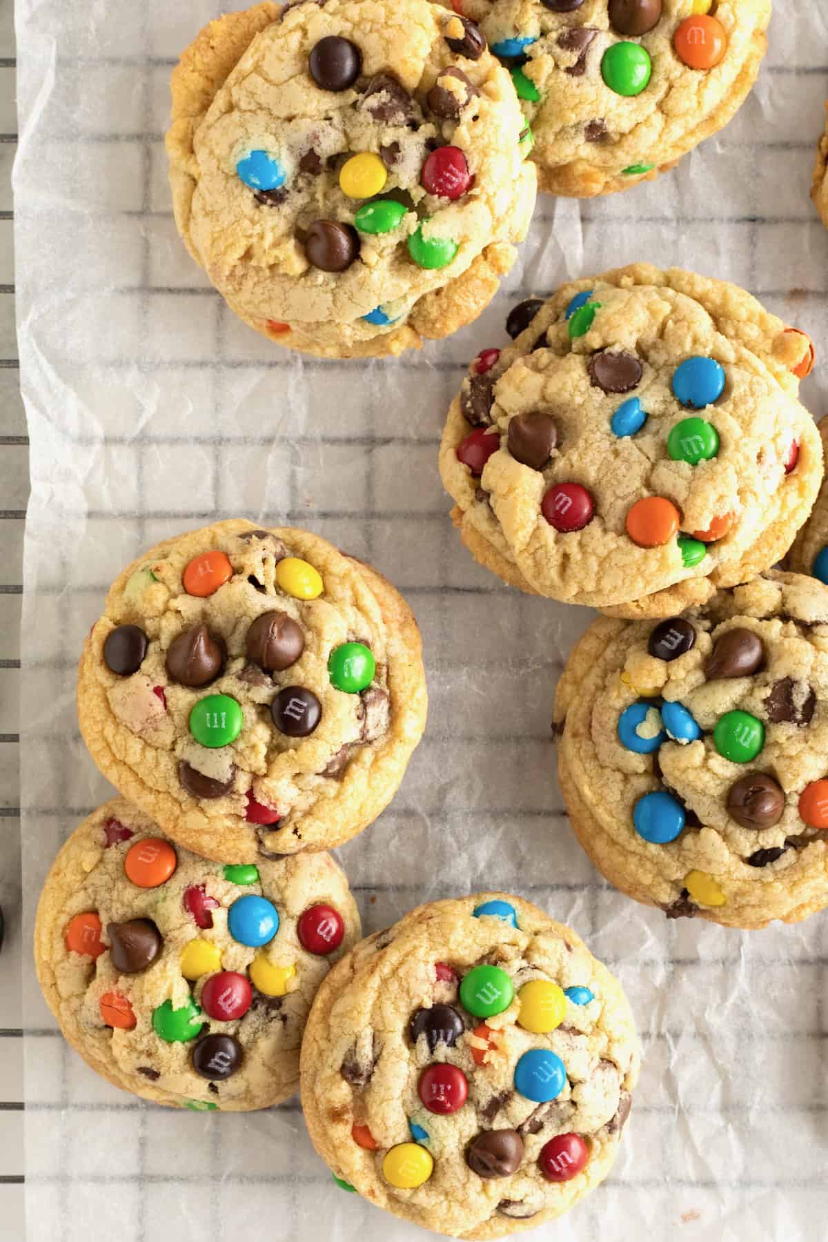 Baked M&M chocolate chip cookies on a parchment lined cooling rack.