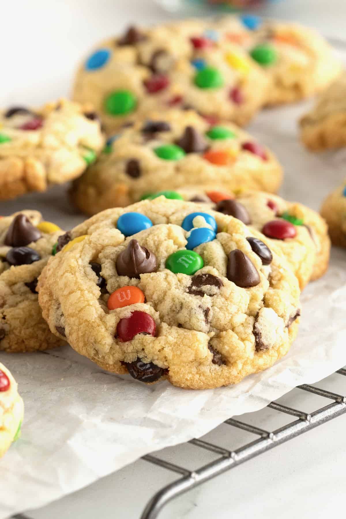 Baked M&M chocolate chip cookies on a parchment lined cooling rack.