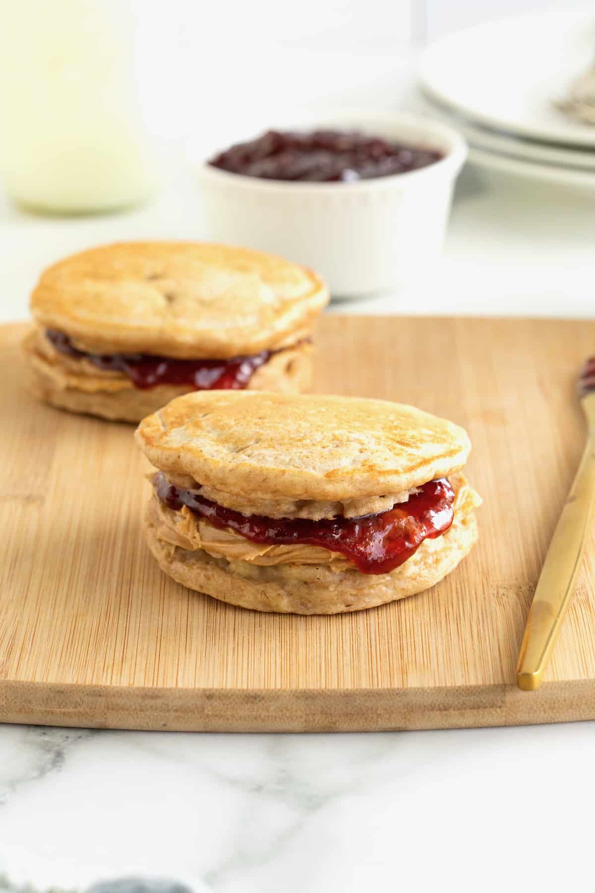 Two banana pancake peanut butter and jelly sandwiches on a wood cutting board.