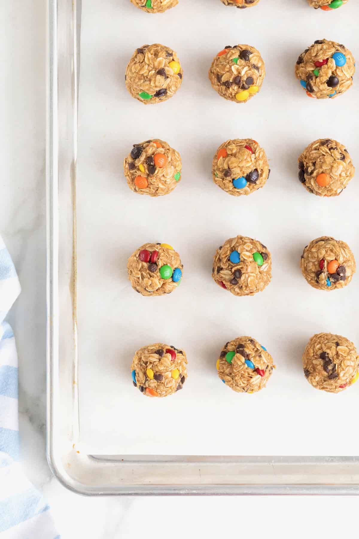 12 no-bake cookie balls with mini M&Ms on a parchment lined baking sheet.