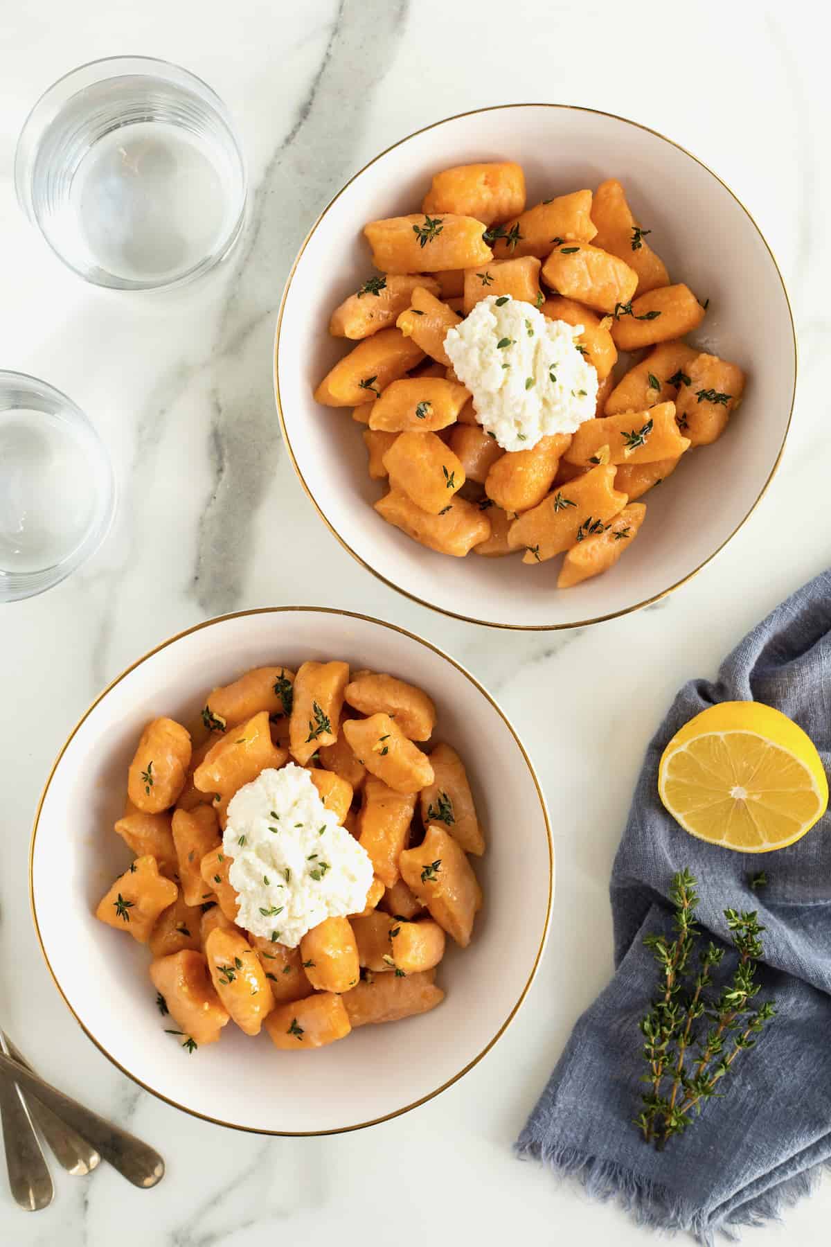 Two gold-rimmed white bowls of sweet potato gnocchi with a dollop of fresh ricotta on top.