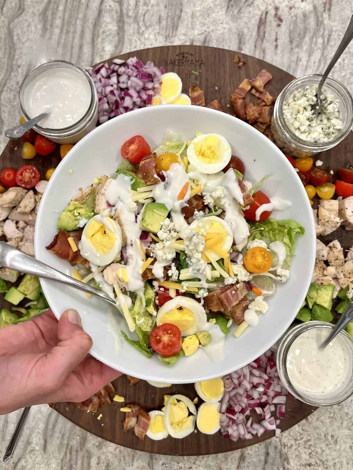 A salad plate with a serving of Cobb Salad topped with hard boiled egg slices, bacon and halved cherry tomatoes.