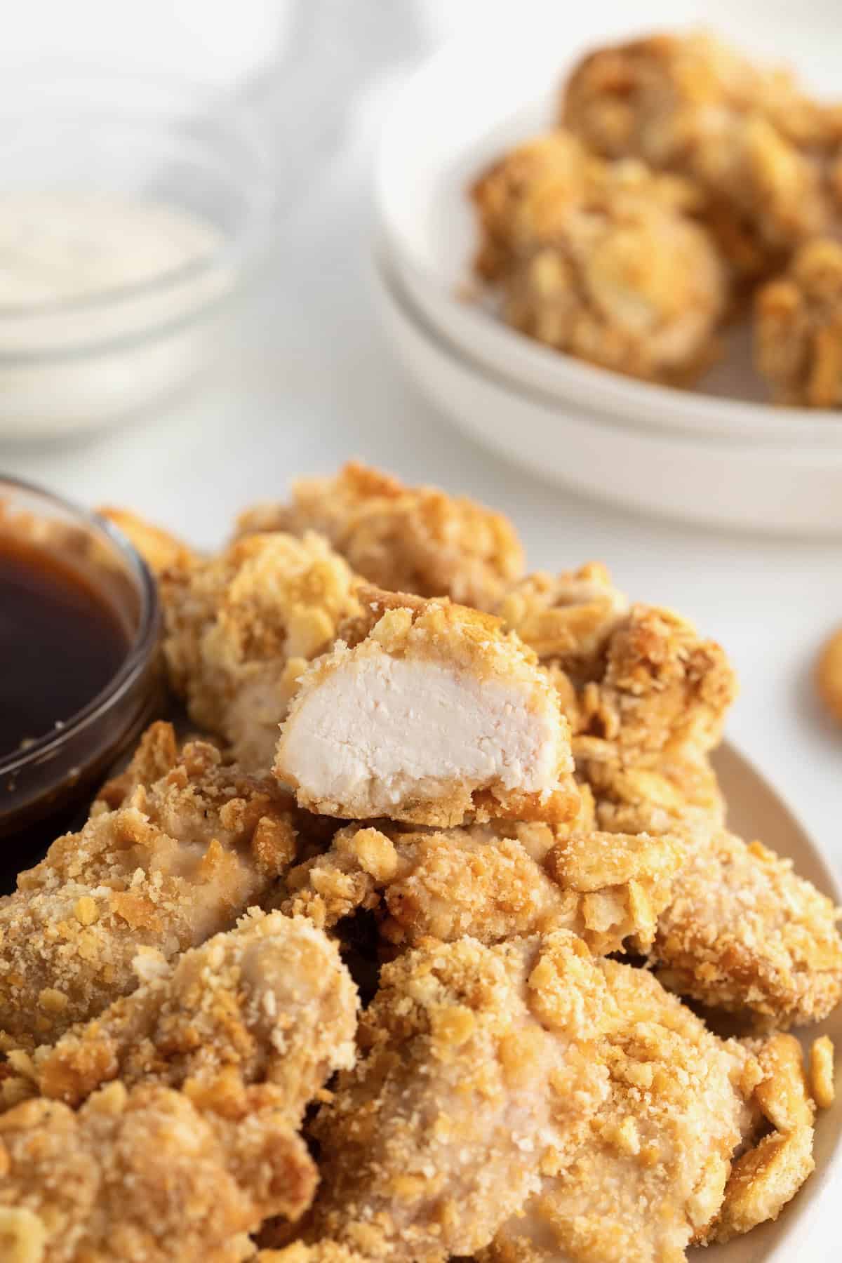 A large white serving plate filled with chicken nuggets. At the top left of the plate is a small glass container of barbecue sauce.
