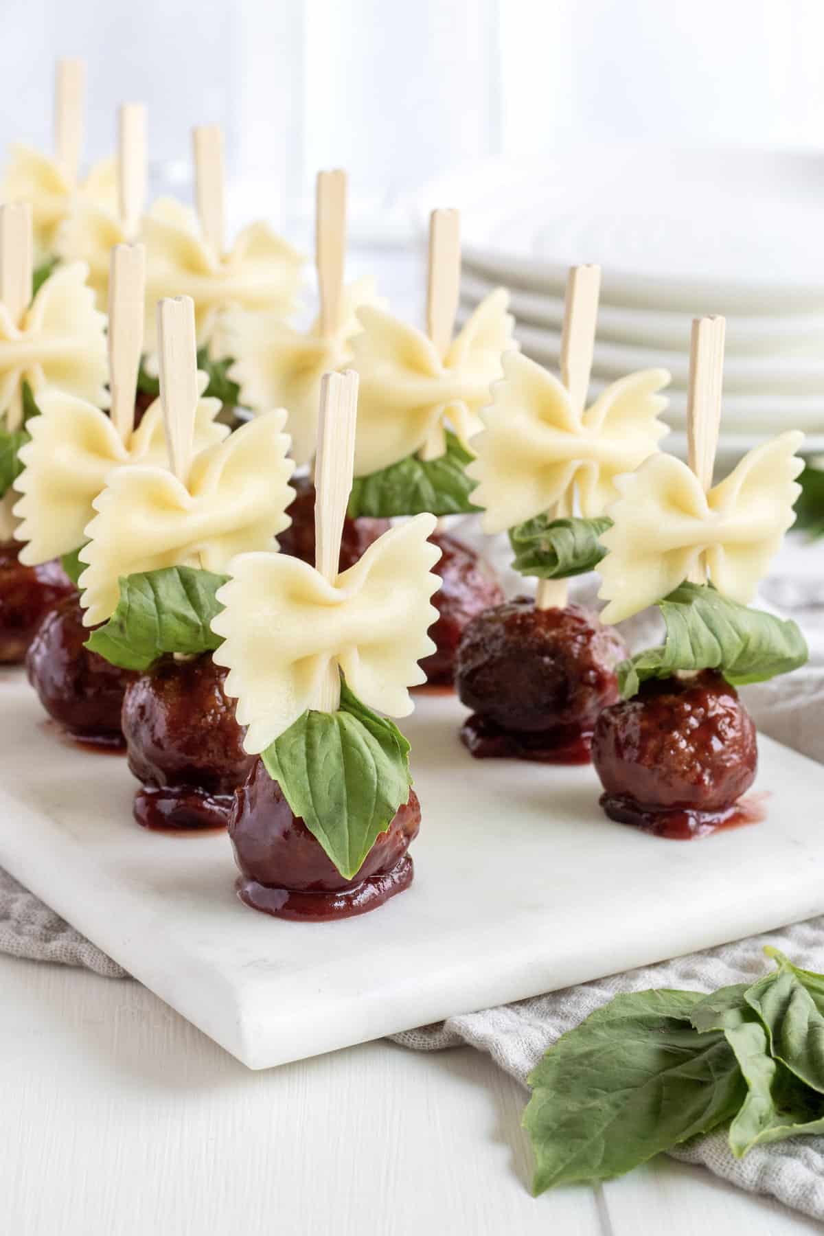 12 bowtie pasta and meatball skewers on a white marble serving plate.