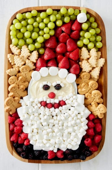 A wood food board decorated with fruit and cookies and marshmallows to look like Santa.