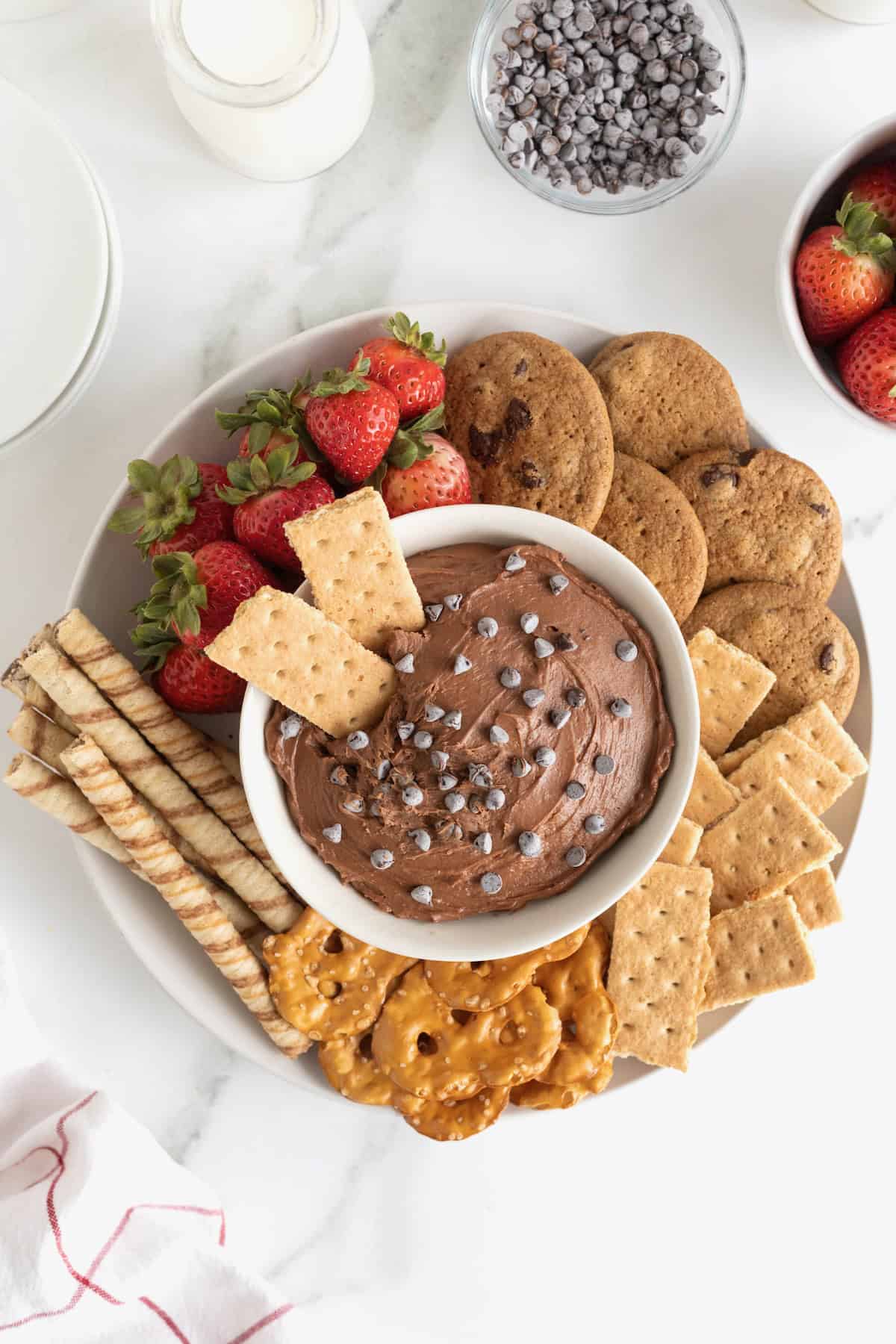 Two pieces of graham cracker sticking out of a white serving bowl of chocolate dip sprinkled with chocolate chips.