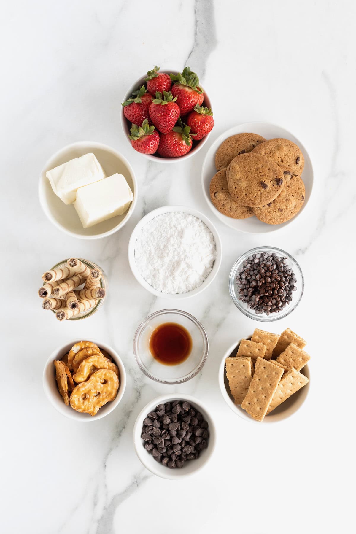 Ingredients to make chocolate cheesecake dip in small glass and white bowls on a white marble counter.