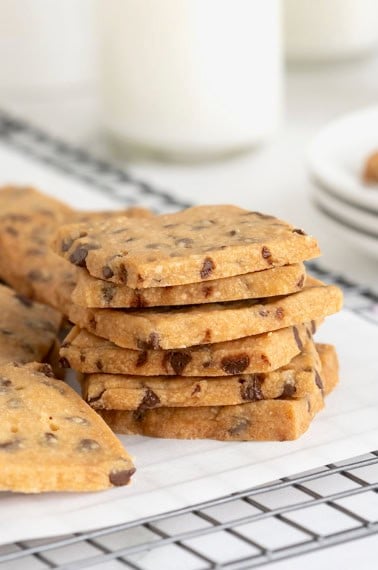 A stack of six chocolate chip cookie crisps on a parchment lined cooling rack.