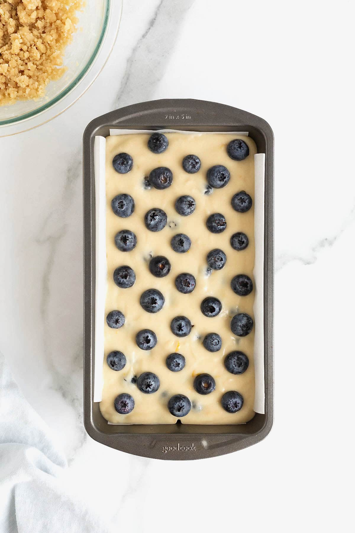 Blueberries on top of lemon blueberry bread batter in a dark aluminum loaf pan.